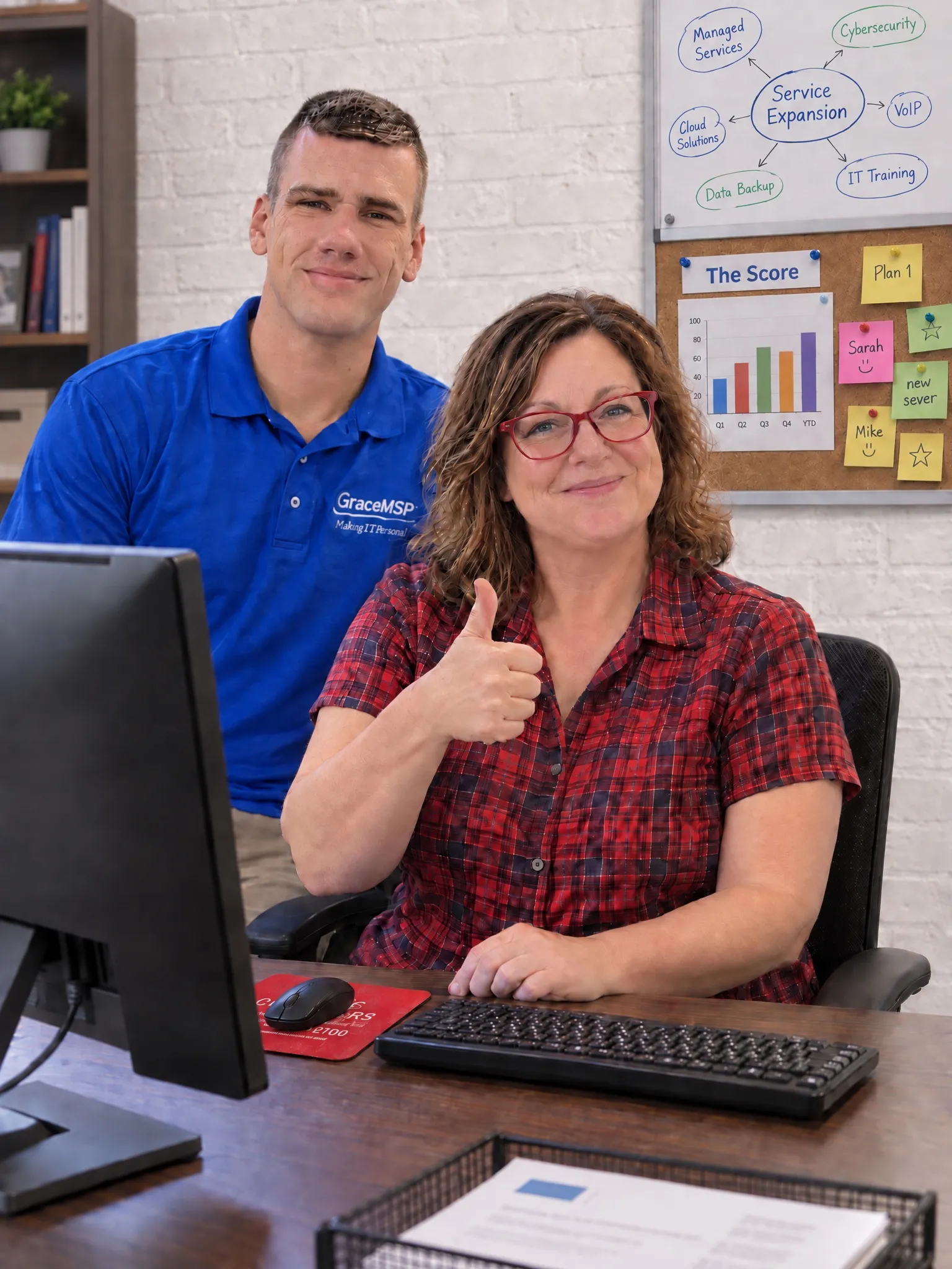 A smiling office worker at her desk alongside a GraceMSP technician.